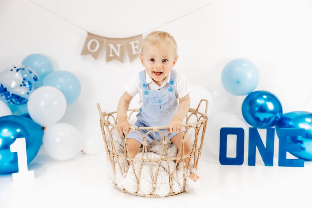 First birthday photo with blue balloons and gold decorative basket.