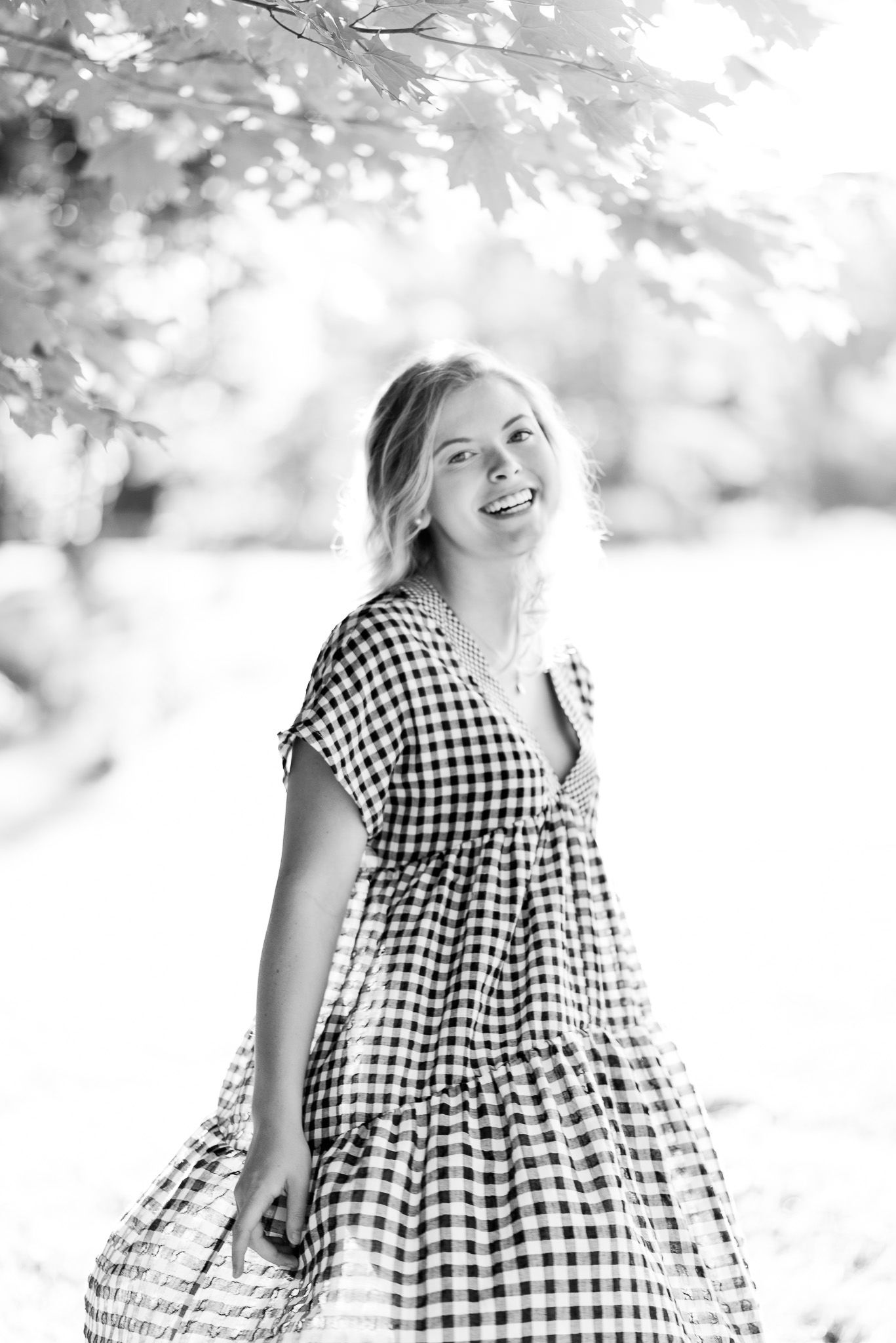 young woman with blonde hair smiling under a tree at sunset for senior pictures at The Marmalade Lily in Cincinnati Ohio