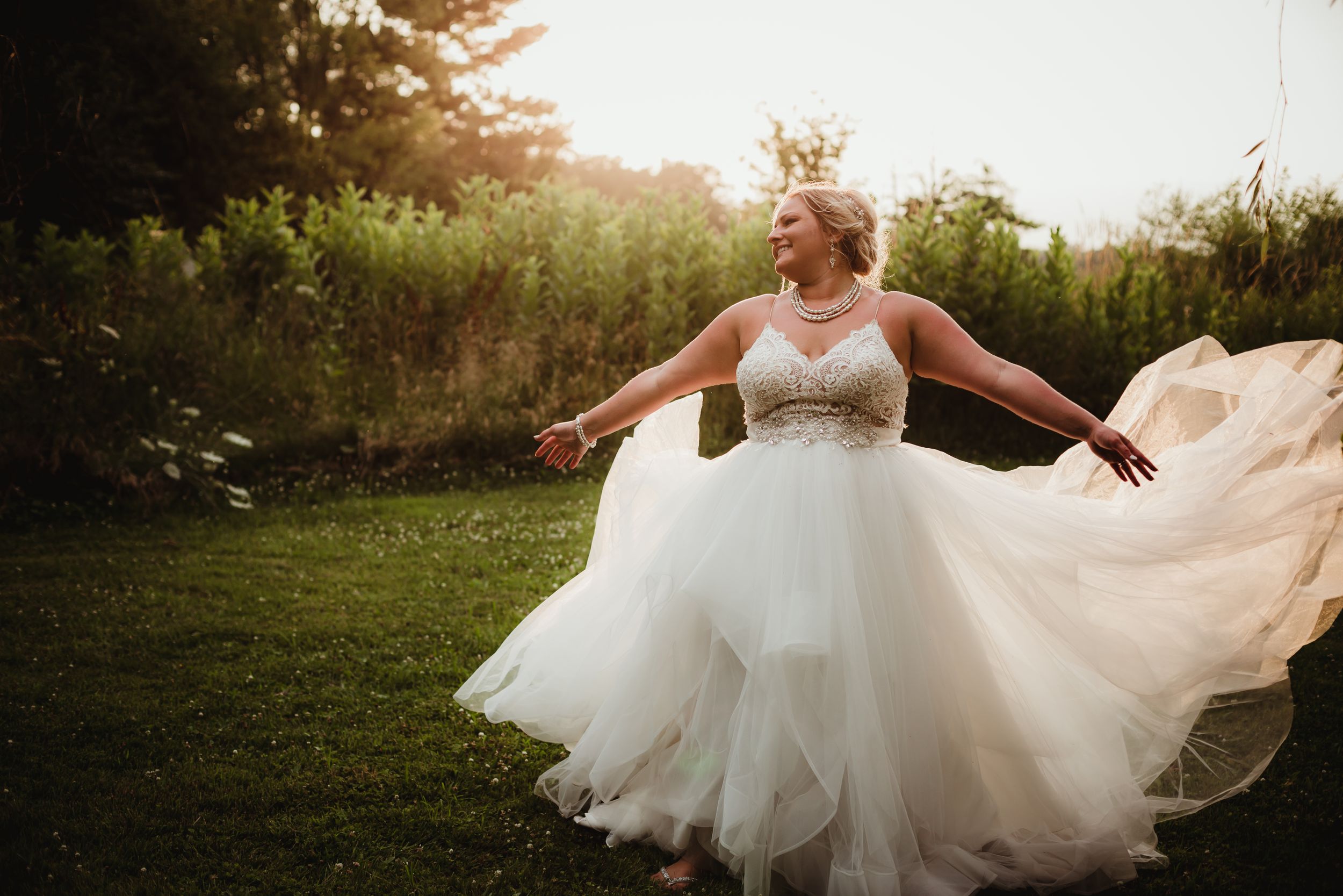 Bride tossing the bottom of her tulle dress into the air. Golden sunset light behind her.
