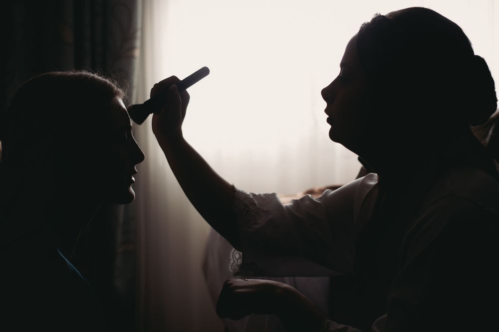Silhouetted figures during makeup application in dramatic backlit composition.