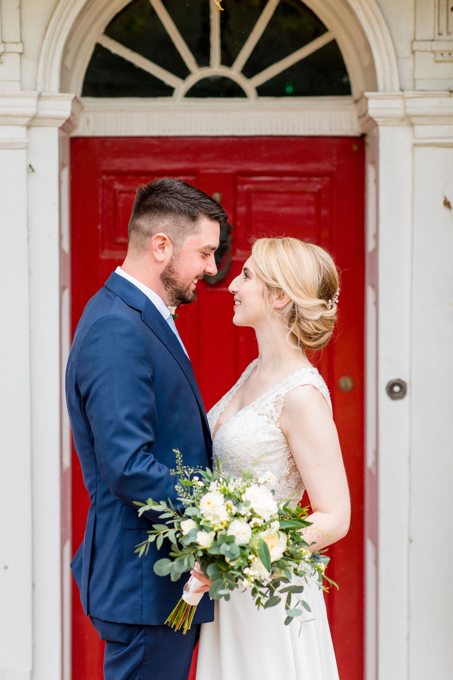 Bride and Groom cuddle infront of red door for wedding photography