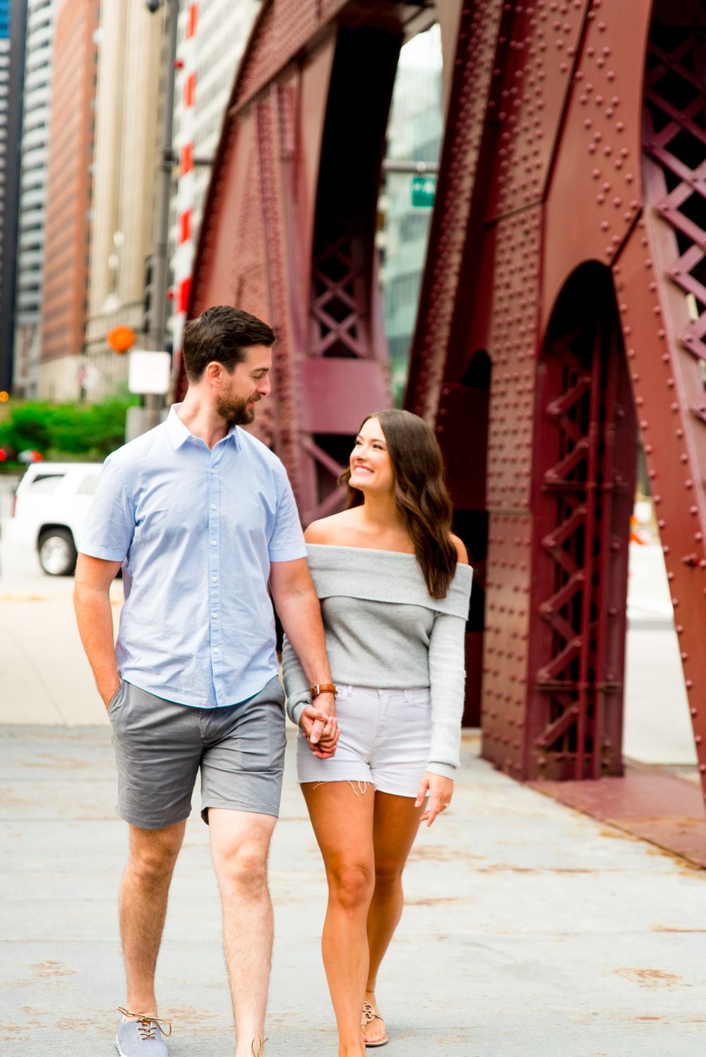 woman in gray sweater and white shorts hugging fiance's arm and walking across LaSalle Street Bridge