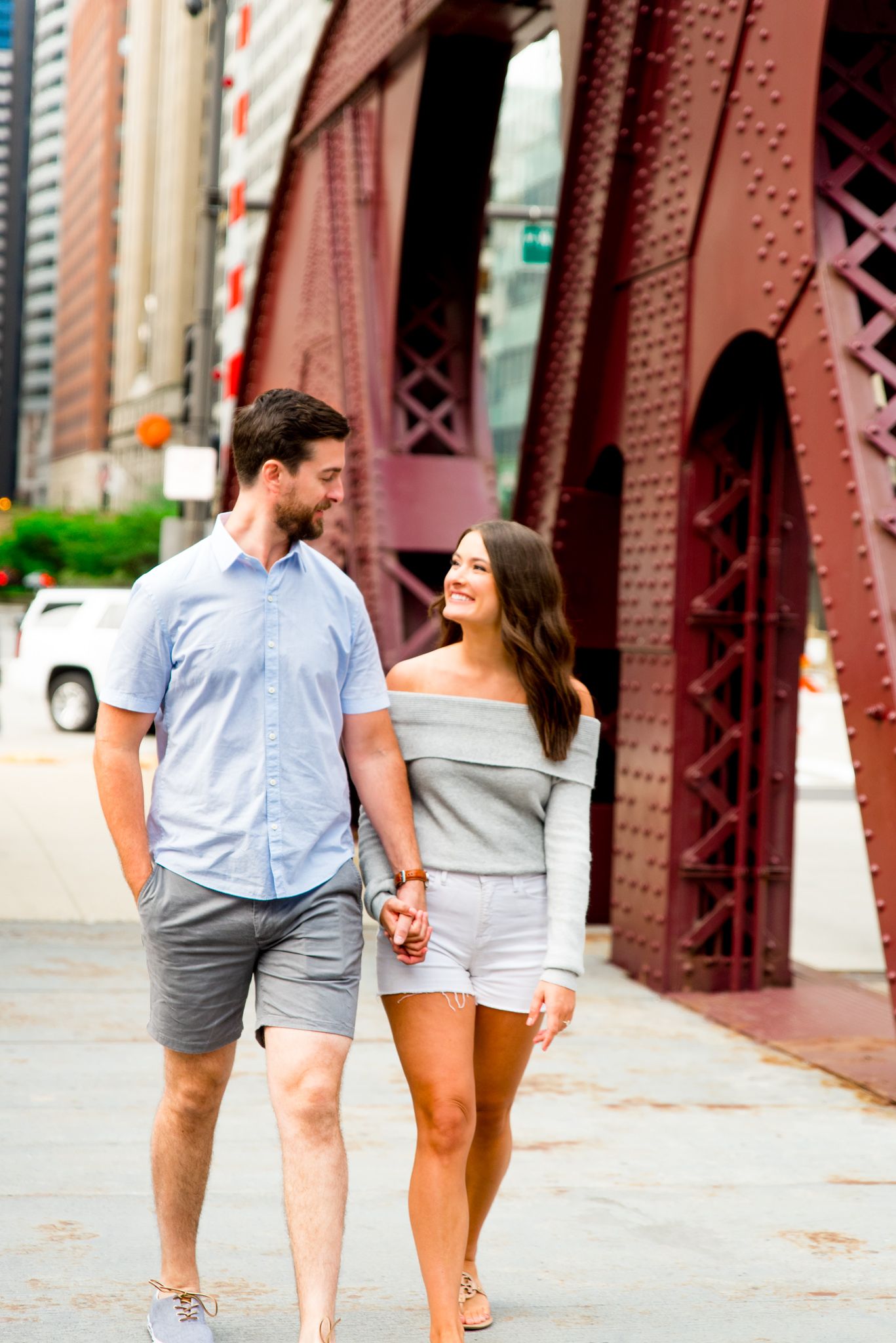 woman in gray sweater and white shorts hugging fiance's arm and walking across LaSalle Street Bridge