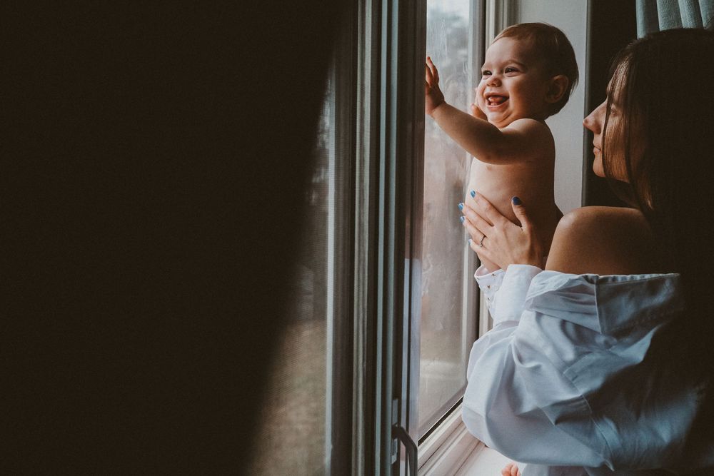 maman qui tient son bébé debout à la fenêtre