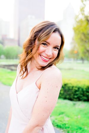 woman in light pink dress and red lipstick smiles over her shoulder in Millennium Park Chicago