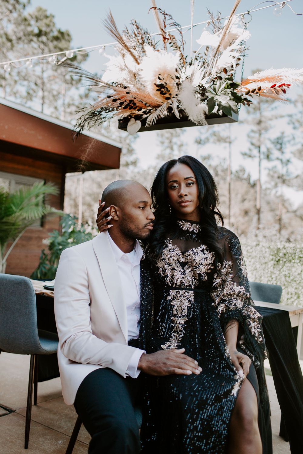 man looking of into the distance as his new wife sits on his lap in front of their bridal table