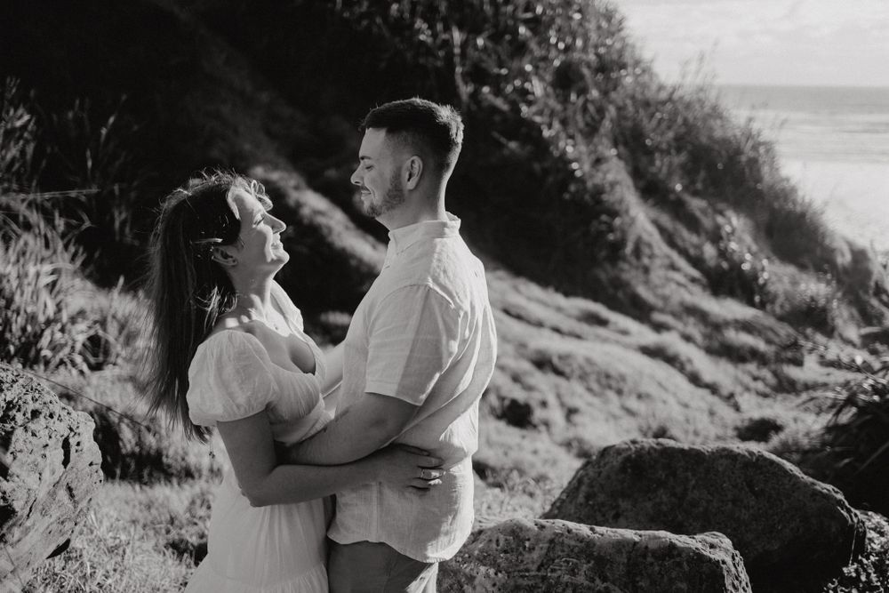 A black and white portrait of a couple embracing on a scenic coastal cliff.