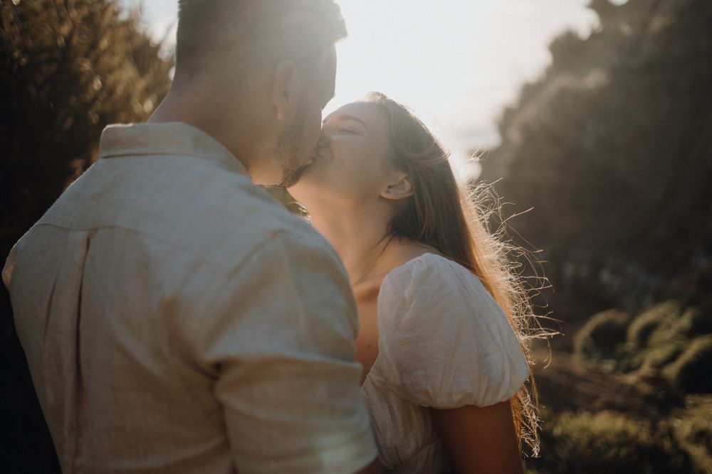 A backlit couple sharing an intimate moment on a sunlit coastal trail.