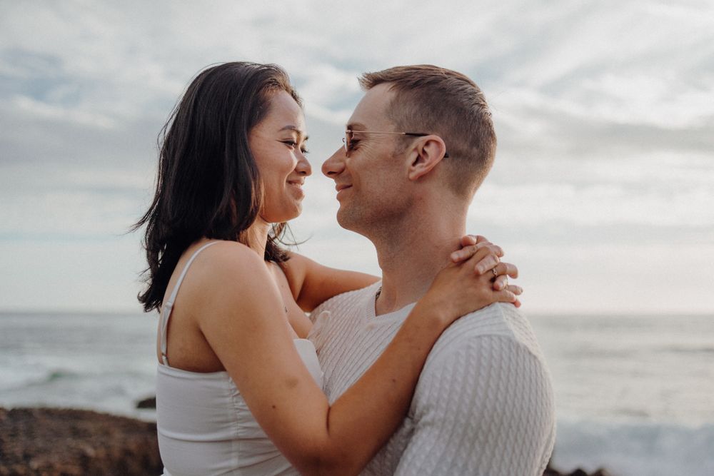 A romantic couple embraces while sharing an intimate moment on a rocky beach at sunset.