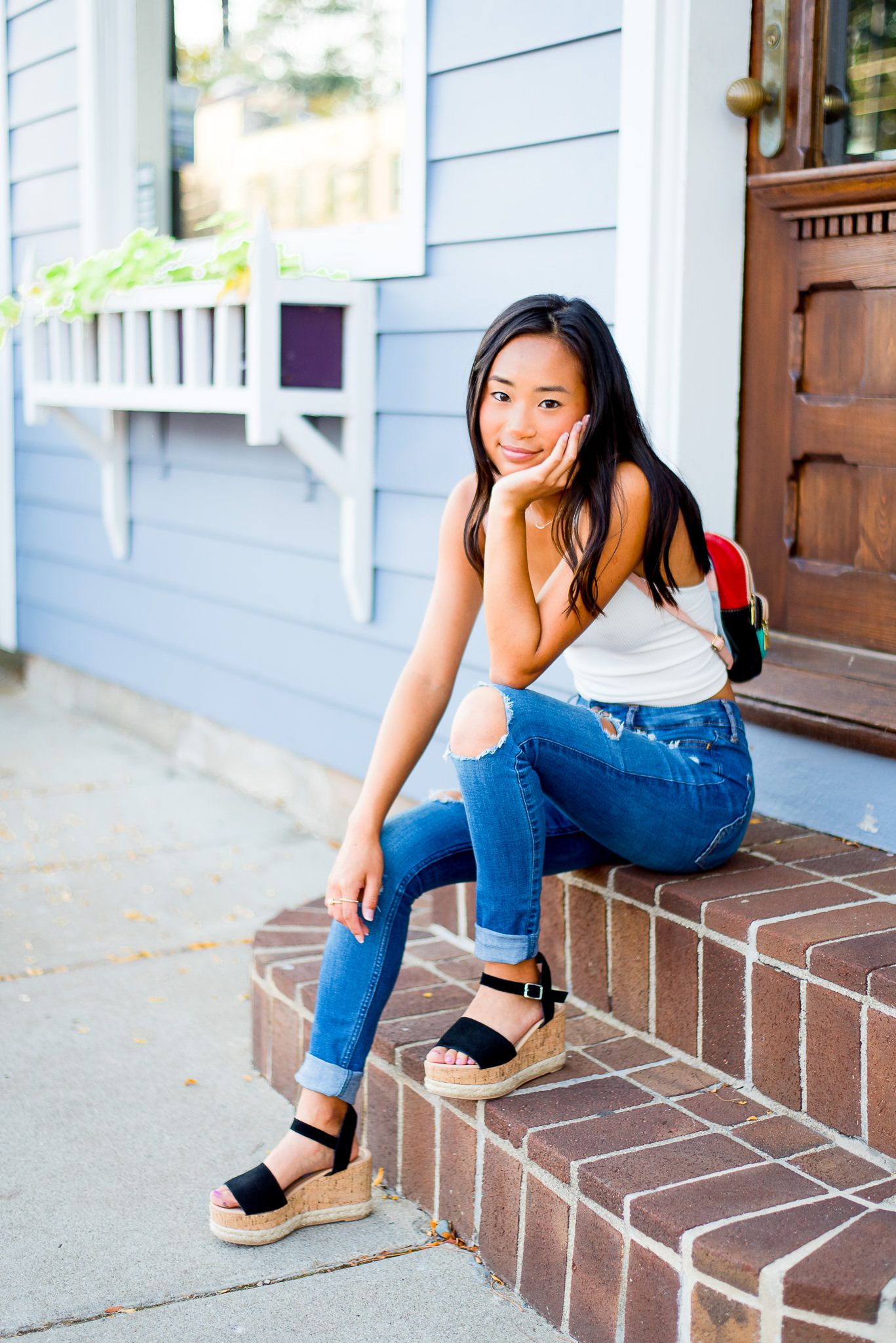 high school senior girl sitting on a stoop smiling with hand on face