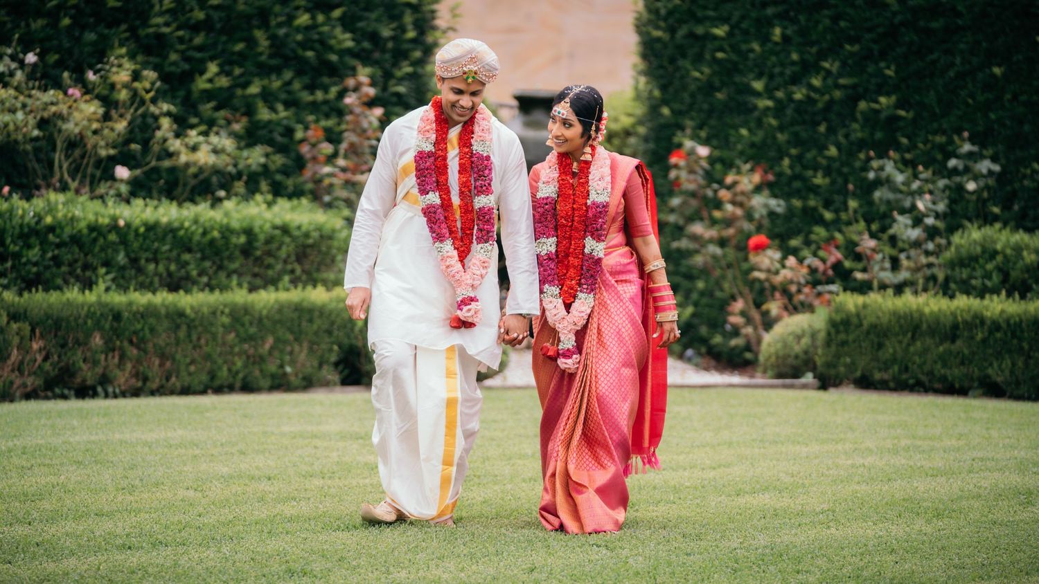 Sri Lankan couple in wedding outfits walking through Miramare Gardens rght after their wedding with flower garlands