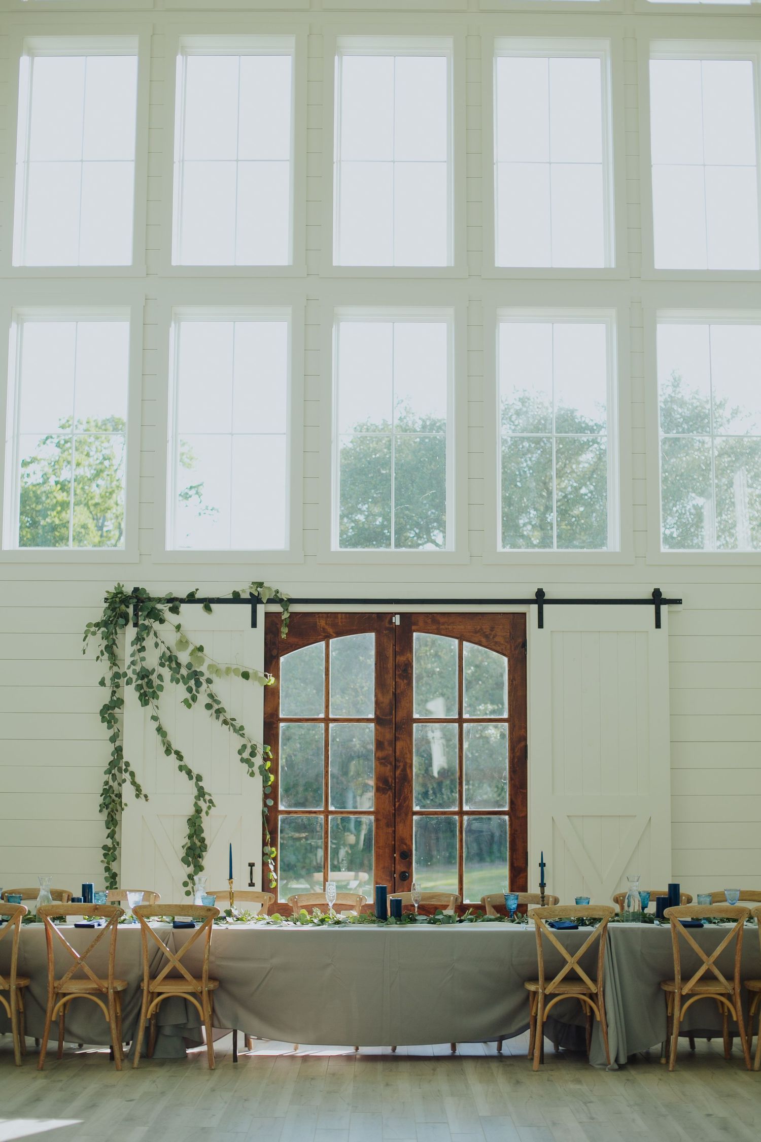 An elegant wedding reception venue with tall windows, barn doors, and table settings.