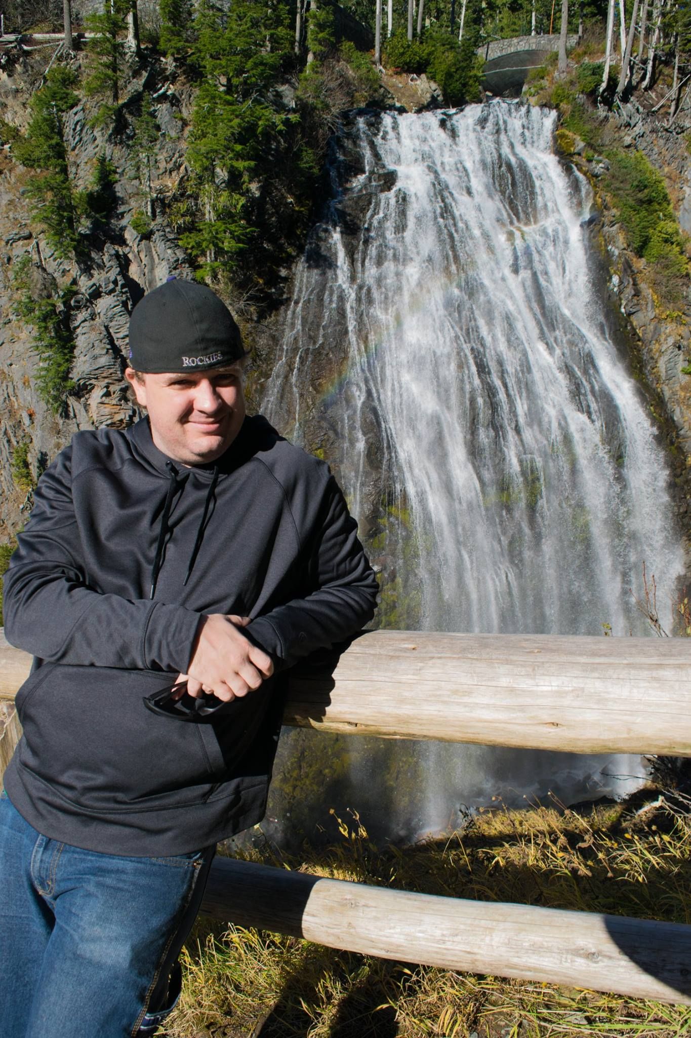 Person poses on wooden bench in front of a scenic waterfall.