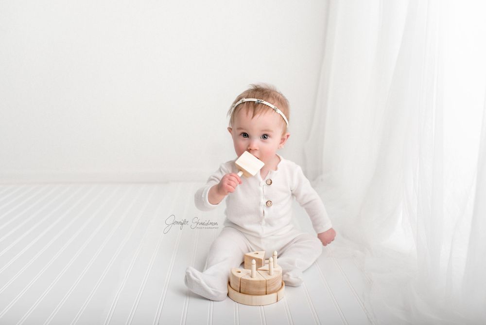 Baby Evelyn looks adorable trying to eat a wooden toy cake during her 1st birthday session in Colorado Springs,