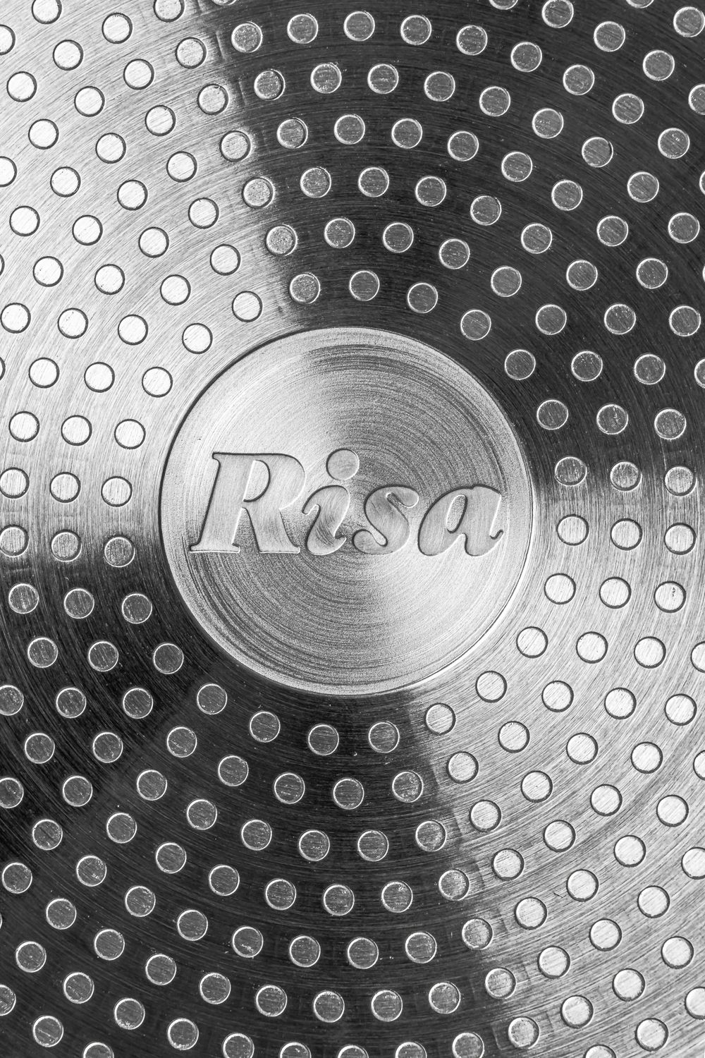 Close-up of a circular metal Risa cookware logo with textured dot pattern background.