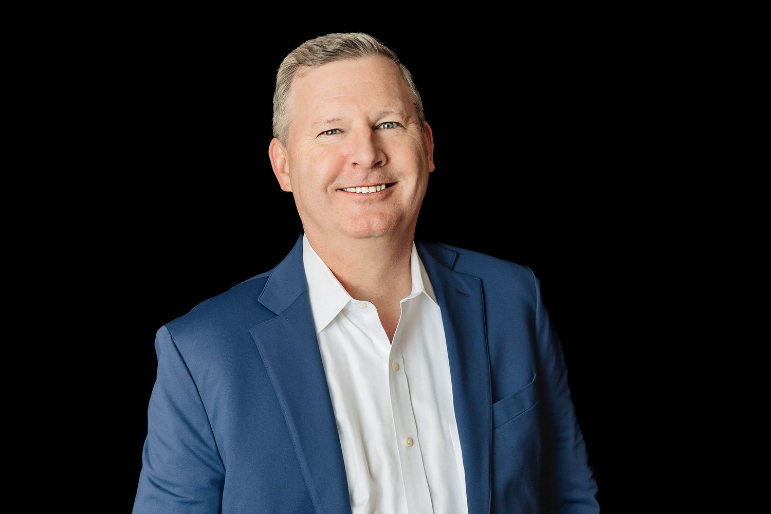 Professional headshot against black background showing person in blue blazer and white dress shirt.