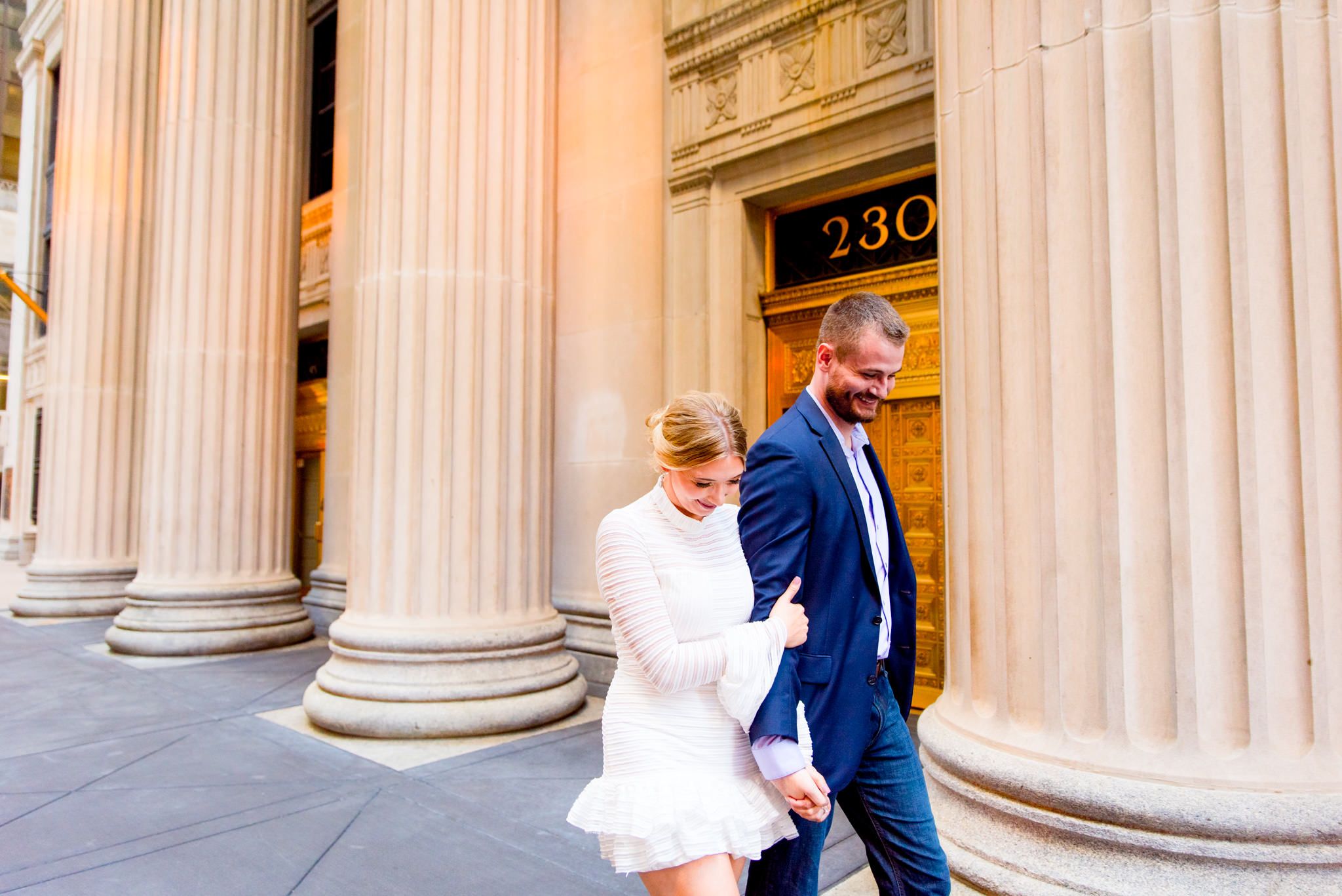 woman in white dress hugging man in navy suit arm both smiling and walking