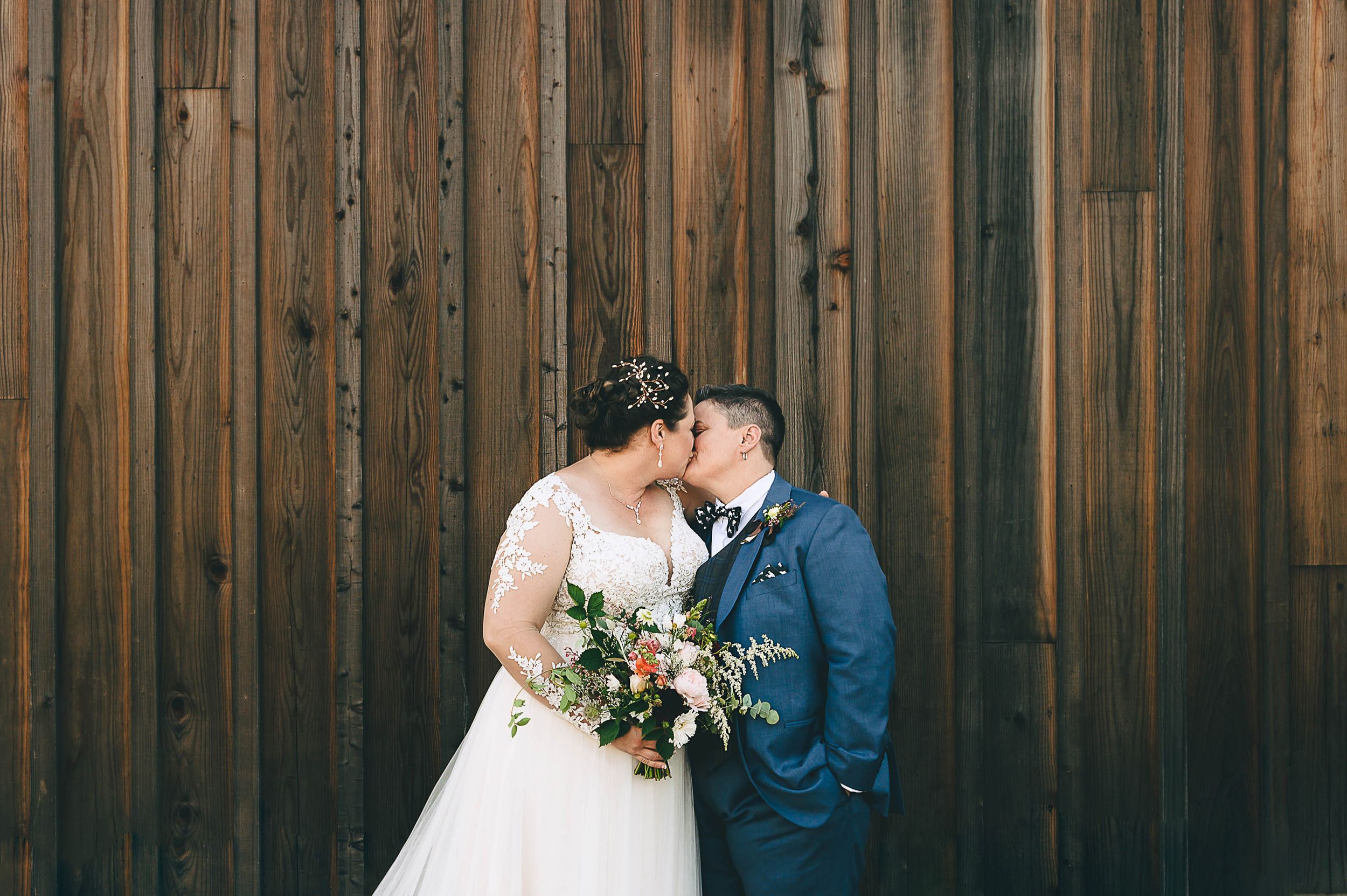 Lesbian brides sharing a kiss outside the barn