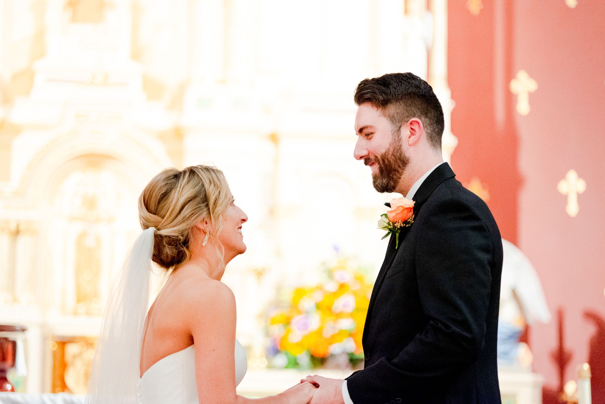 blonde bride with updo and veil smiling at her groom with brunette hair and beard in church
