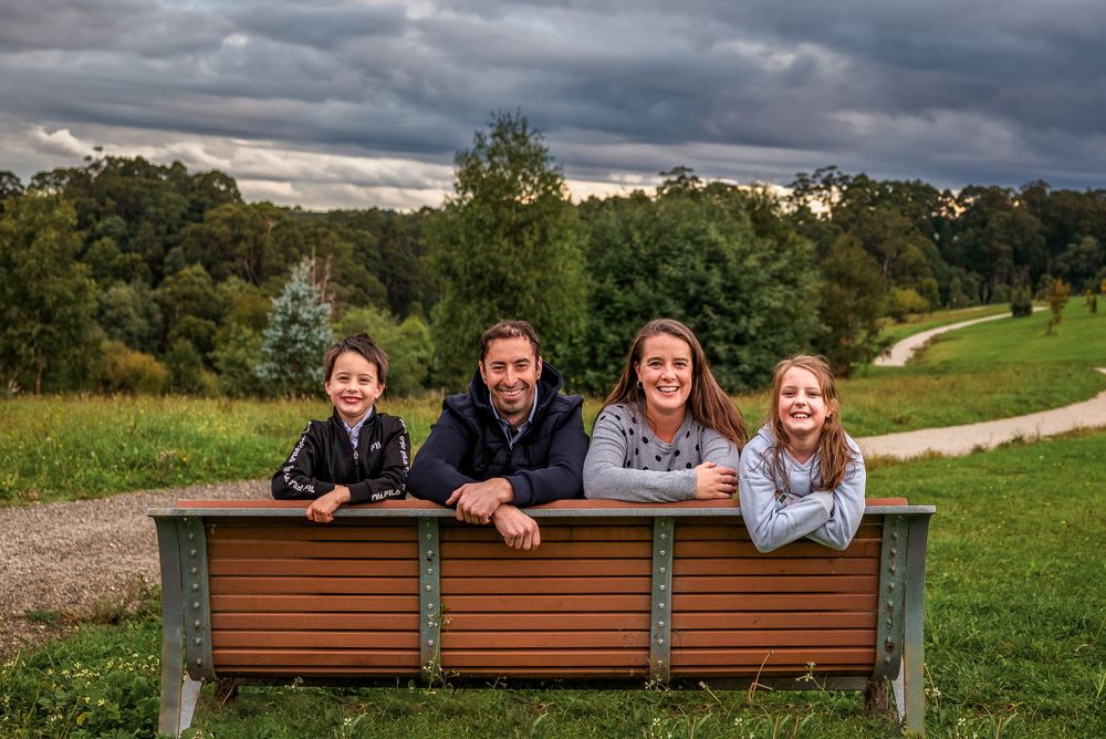 Family of four looking over back of park bench with storm clouds behind