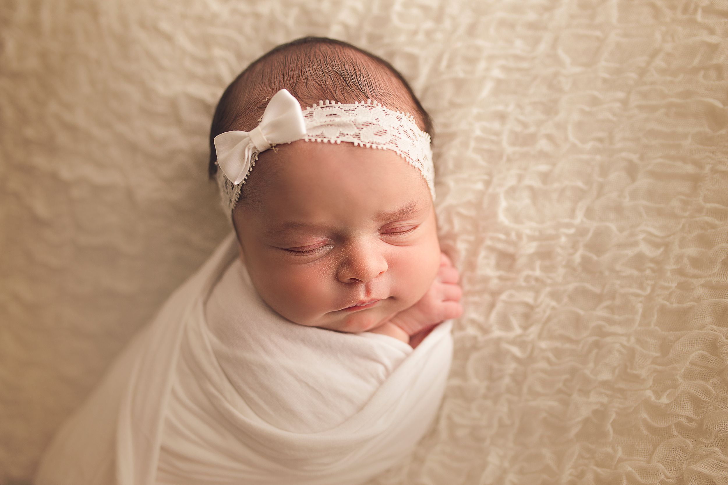 baby wrapped in white blanket with headband close up image