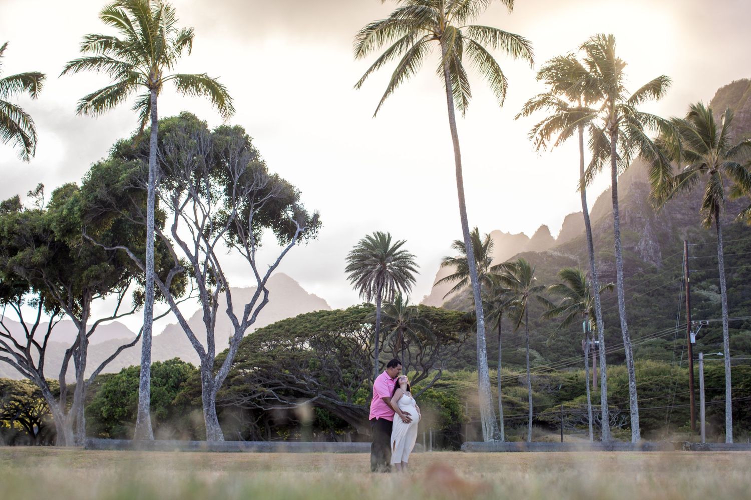 Couple standing among palm trees at sunset in tropical Hawaiian landscape.