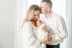 Mother holds her newborn sleeping on her chest as her husband kisses her head.