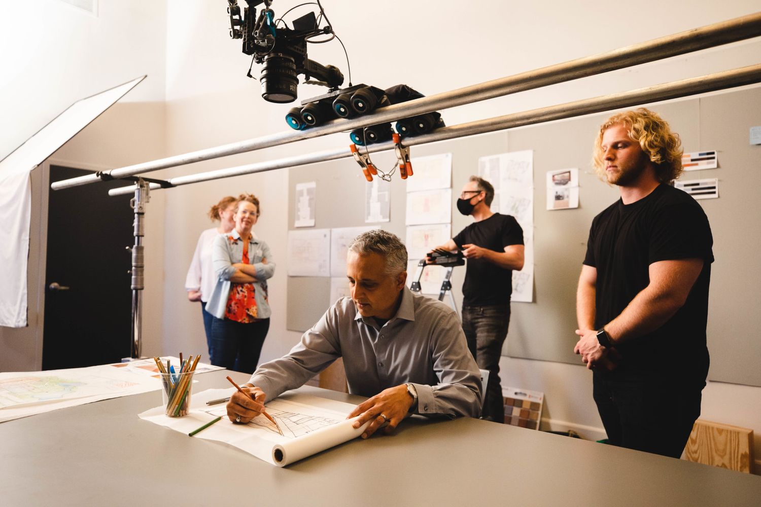 Film crew working in a studio setting with lighting equipment and production gear around a desk.