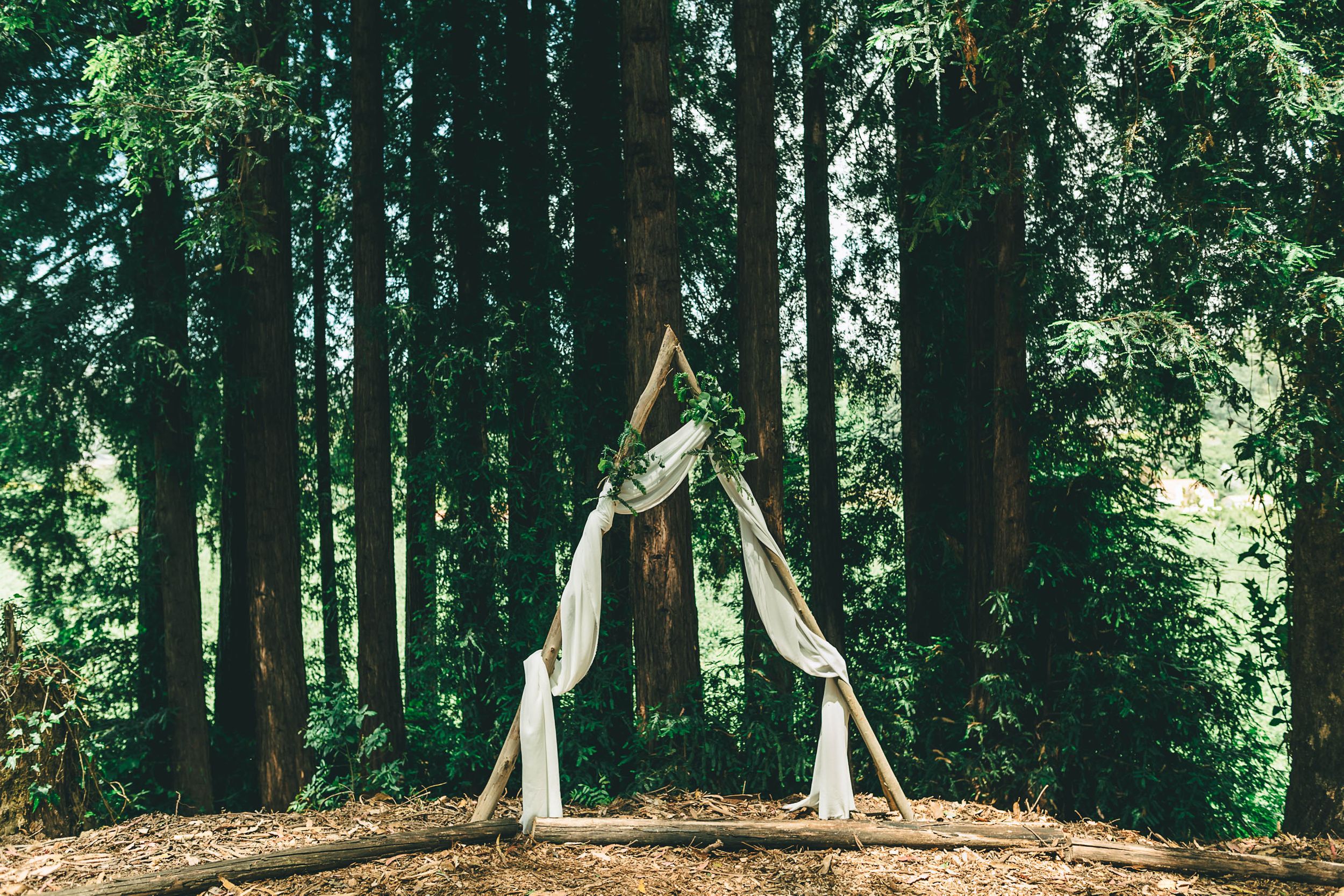 Triangular wooden wedding arch surrounded by redwood trees