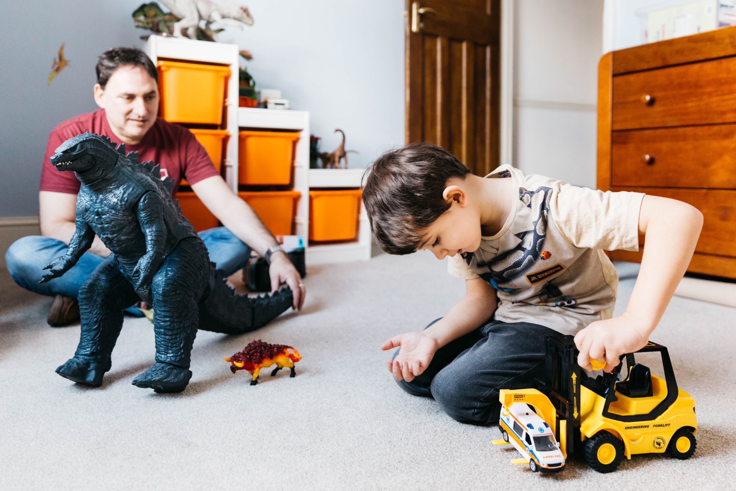 dad and son playing with dinosaurs cars in bedroom