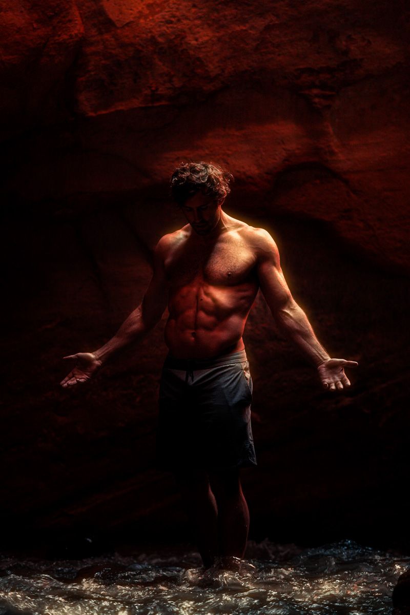 humbled muscled holy man ammon with arms out glowing in a slot canyon