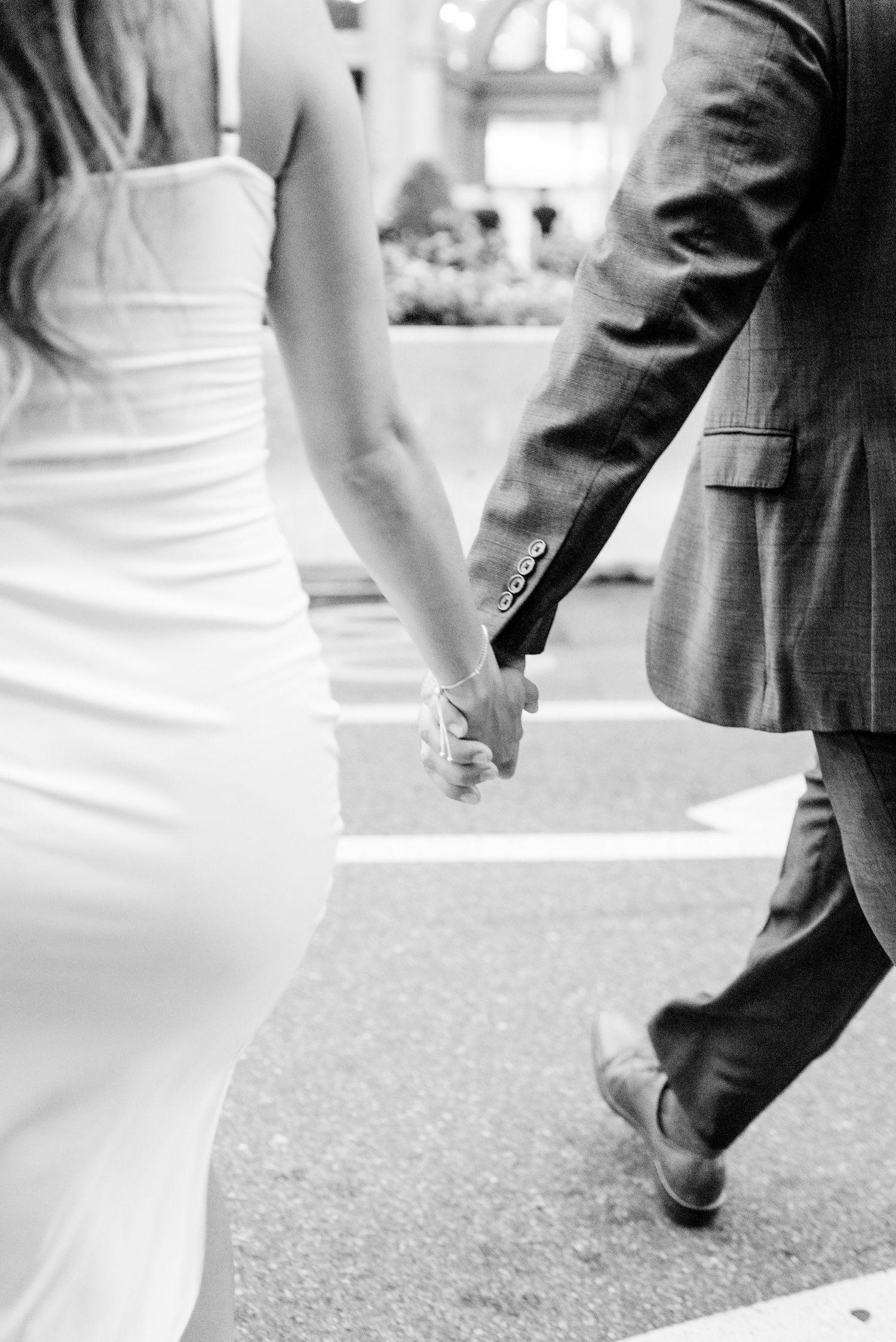 woman in white dress and man in suite holding hands walking through Flatiron District NYC for engagement photos