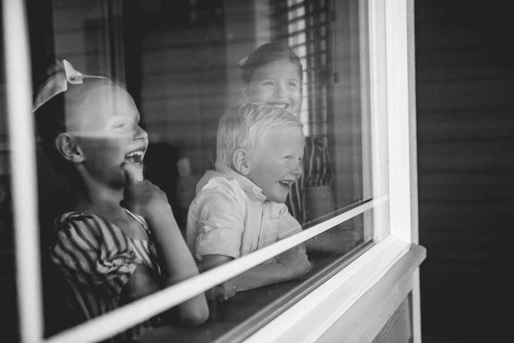 three siblings looking out their dining room window laughing