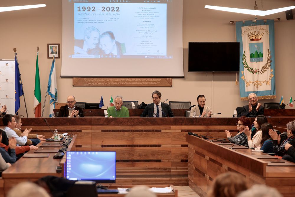 Conference room meeting with presentation screen and Italian flags displayed.