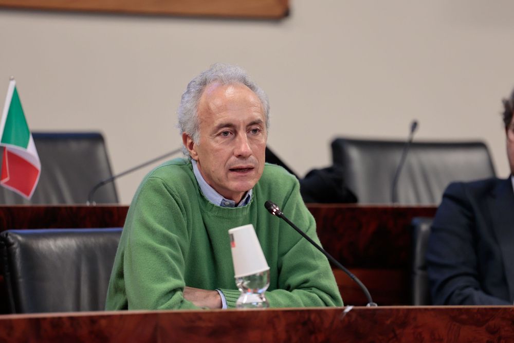 Speaker in a green sweater addresses audience at a conference podium.