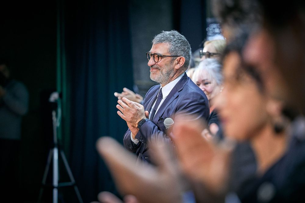 Man in dark suit clapping during formal gathering.