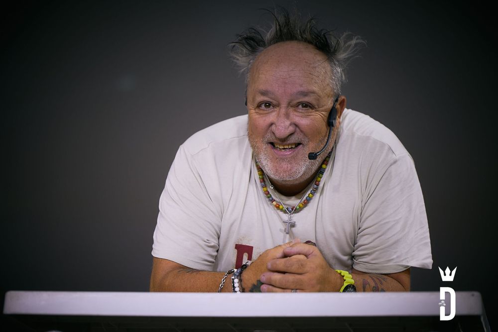 Performer wearing headset and white t-shirt smiles during stage show against dark background.