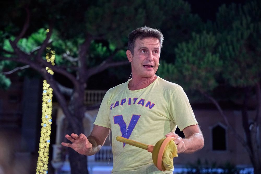 Performer gesturing while wearing a yellow Varitan V t-shirt during an outdoor show.