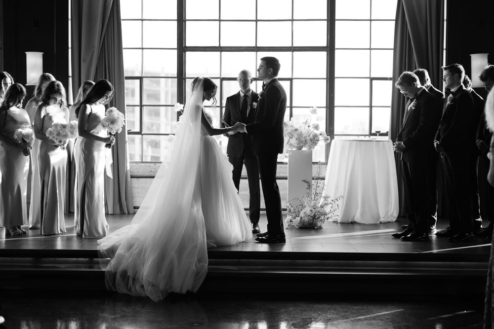 Silhouette of wedding ceremony in venue with large windows and elegant lighting.