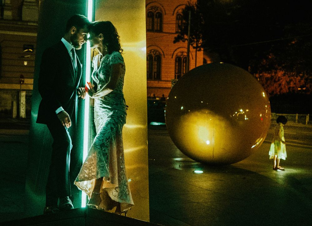 Romantic nighttime scene with couple near glowing lights and large golden sphere in urban setting.