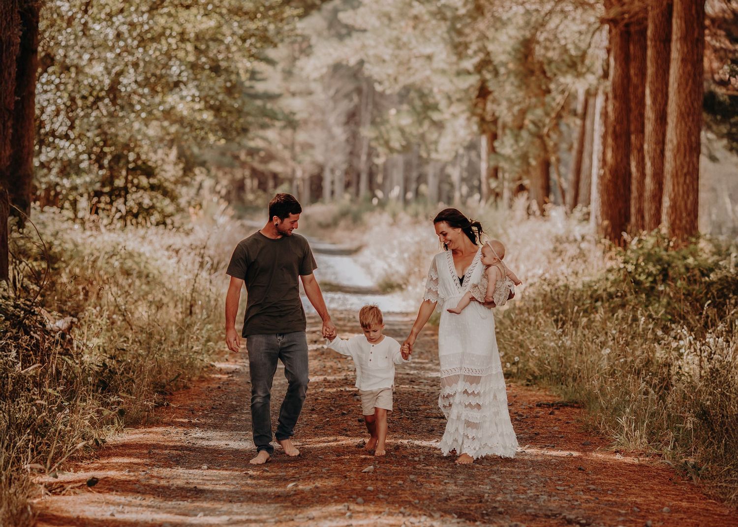 Family walks hand in hand down a sunlit forest path lined with tall trees.