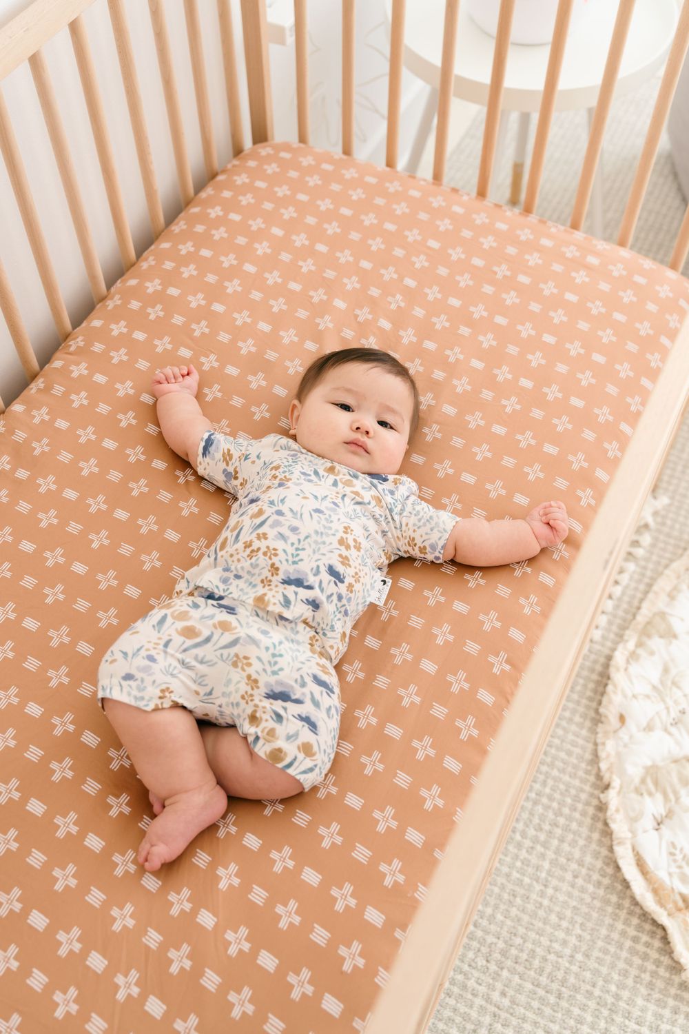 Baby lying on peach-colored fitted crib sheet with cross pattern.