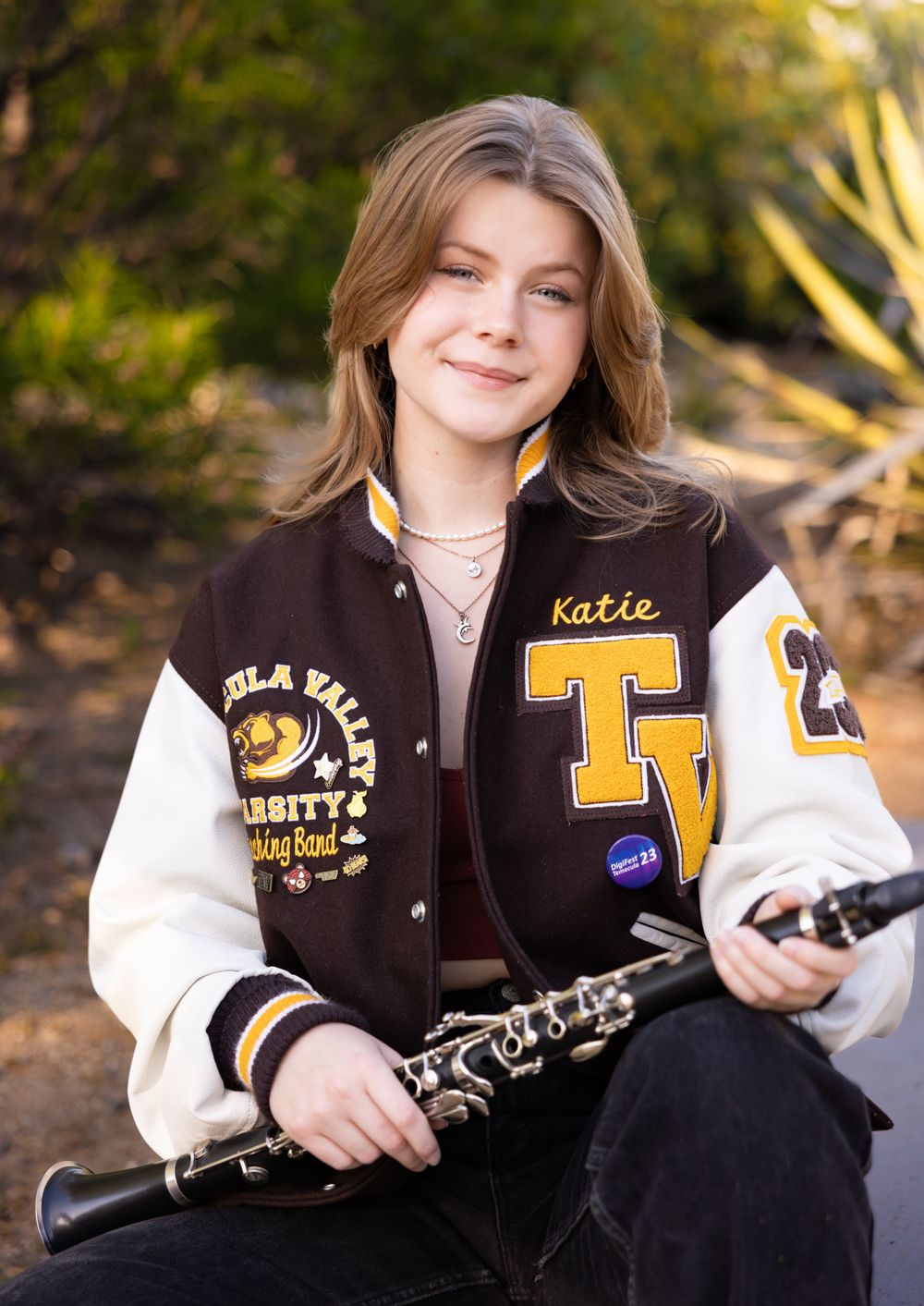 Student musician poses with clarinet wearing brown and white varsity letterman jacket.