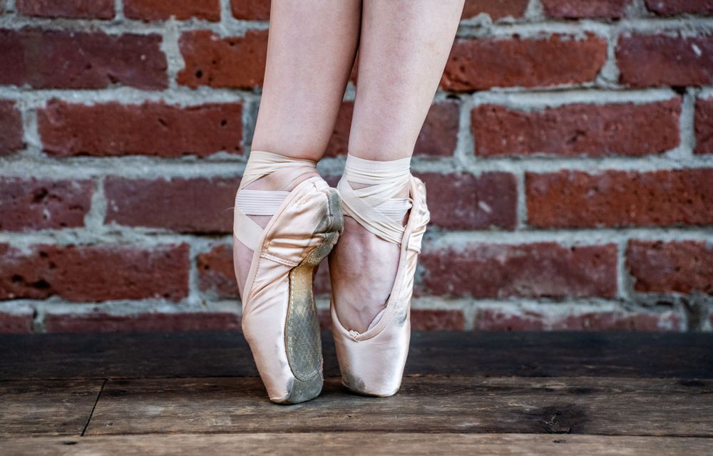 Ballet pointe shoes resting en pointe against brick wall background.