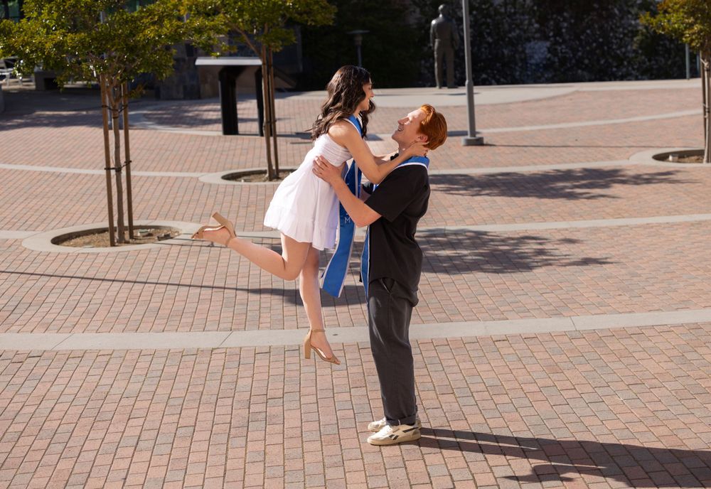 Celebratory graduation lift pose between two people on brick plaza.