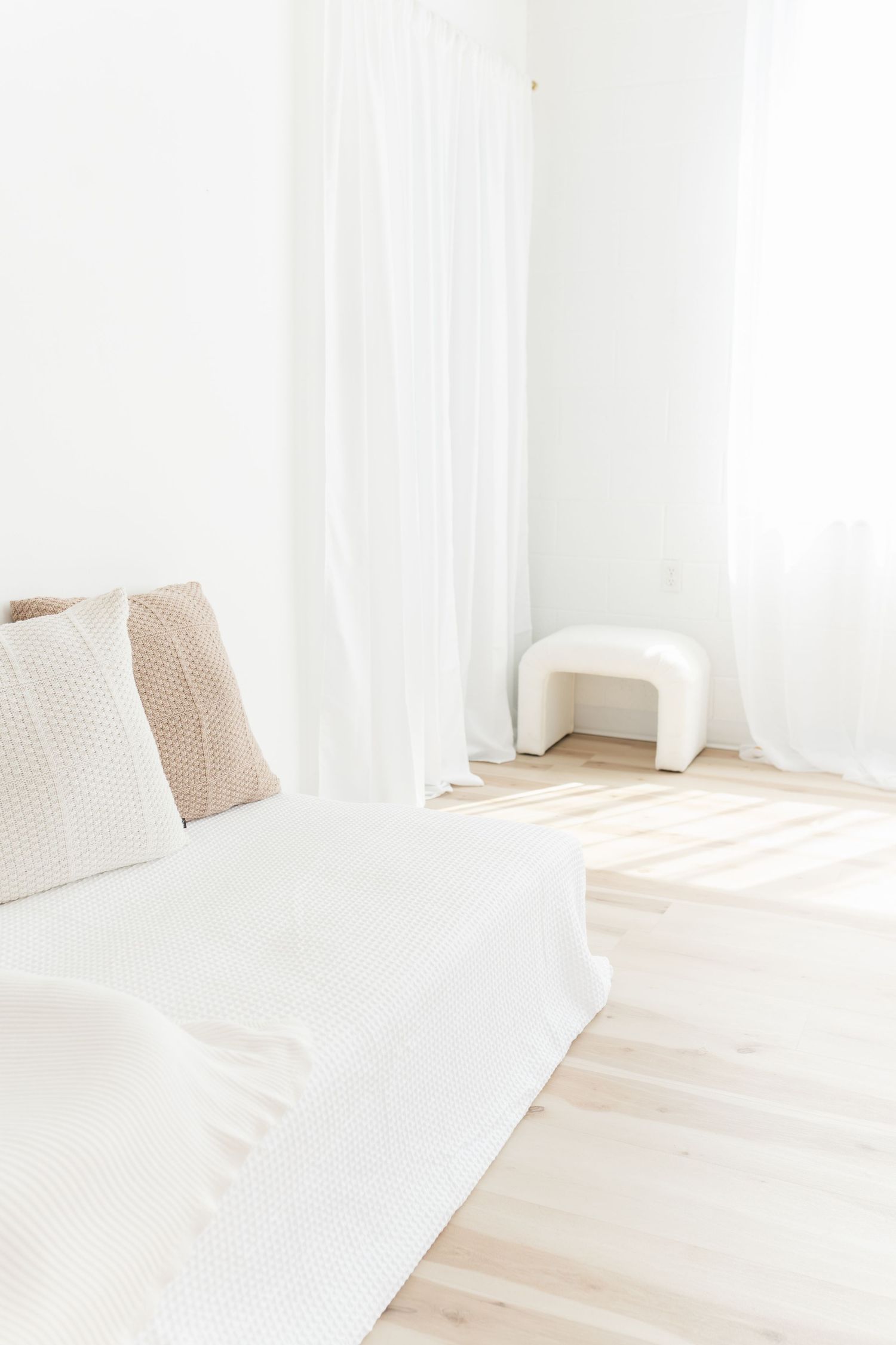 Minimalist white room interior with natural light featuring a white couch and wooden flooring.