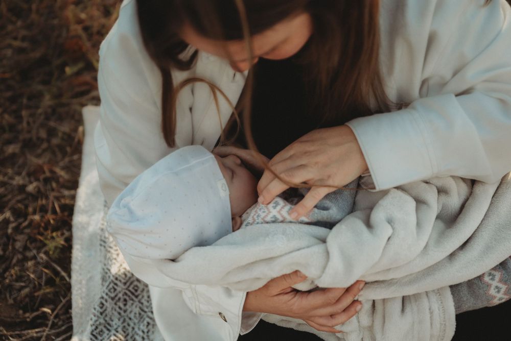 A tender moment with a swaddled newborn being cradled on a blanket outdoors.