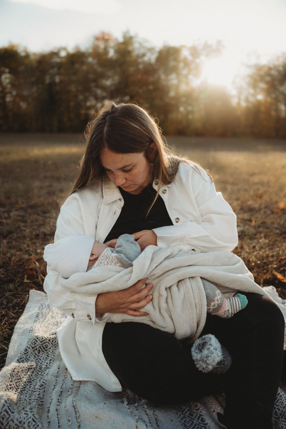 A peaceful outdoor portrait of parent and newborn on a blanket during golden hour.