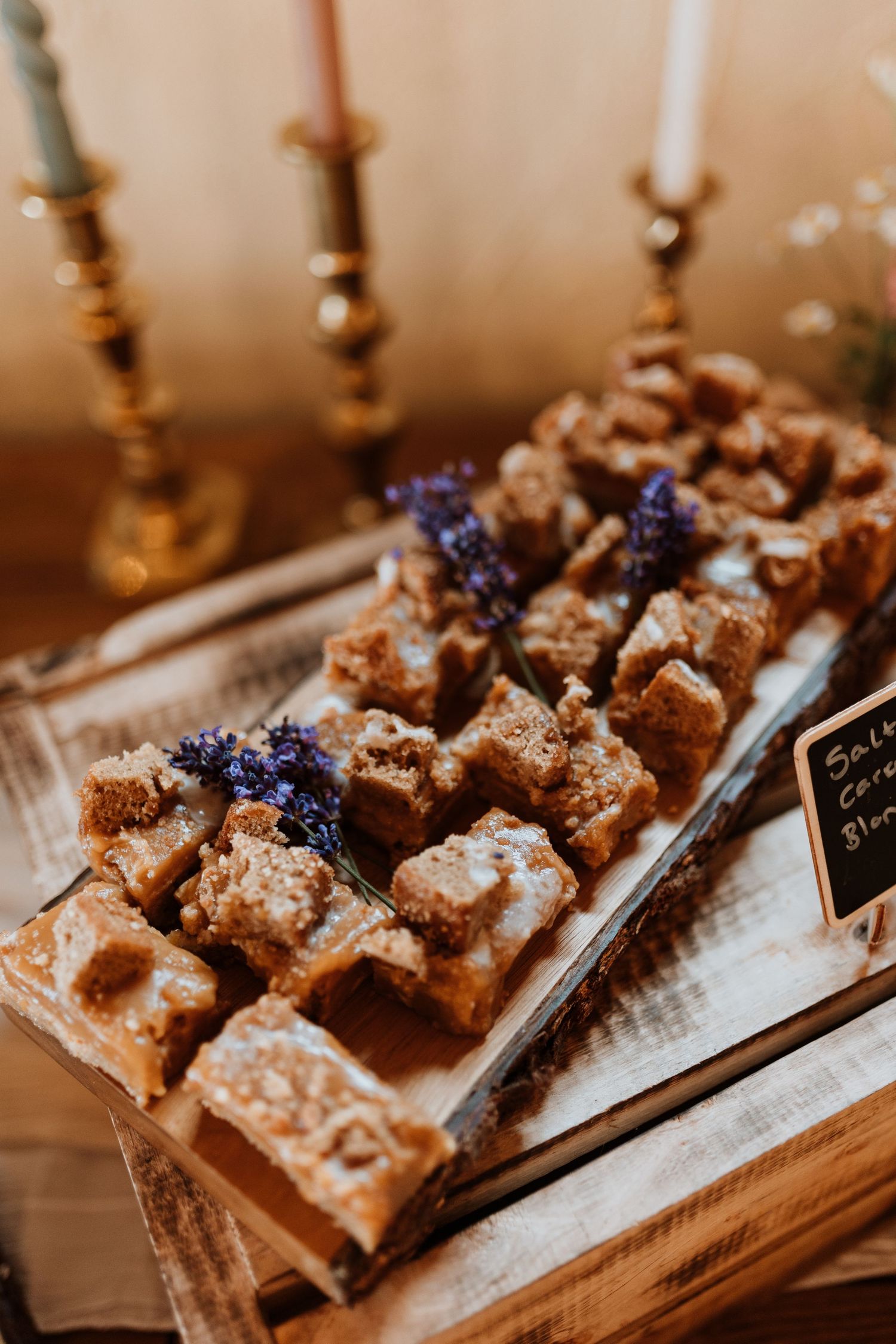 Rustic dessert display with powdered pastries garnished with sprigs of lavender on a wooden serving tray with gold candlesticks.