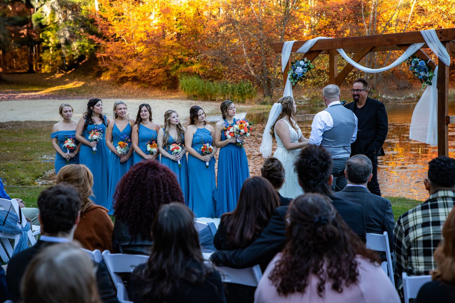 A joyous moment during an outdoor wedding ceremony under a floral arch on a sunny autumn day.
